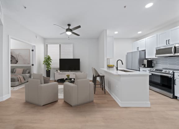 a living room with couches and a kitchen and a ceiling fan